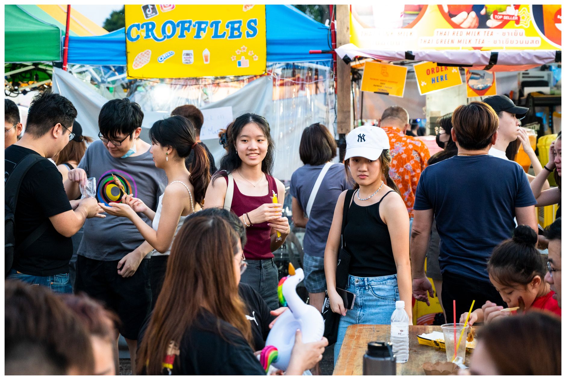 Overhead view of a vibrant global food market with various street food stalls and people sampling dishes.