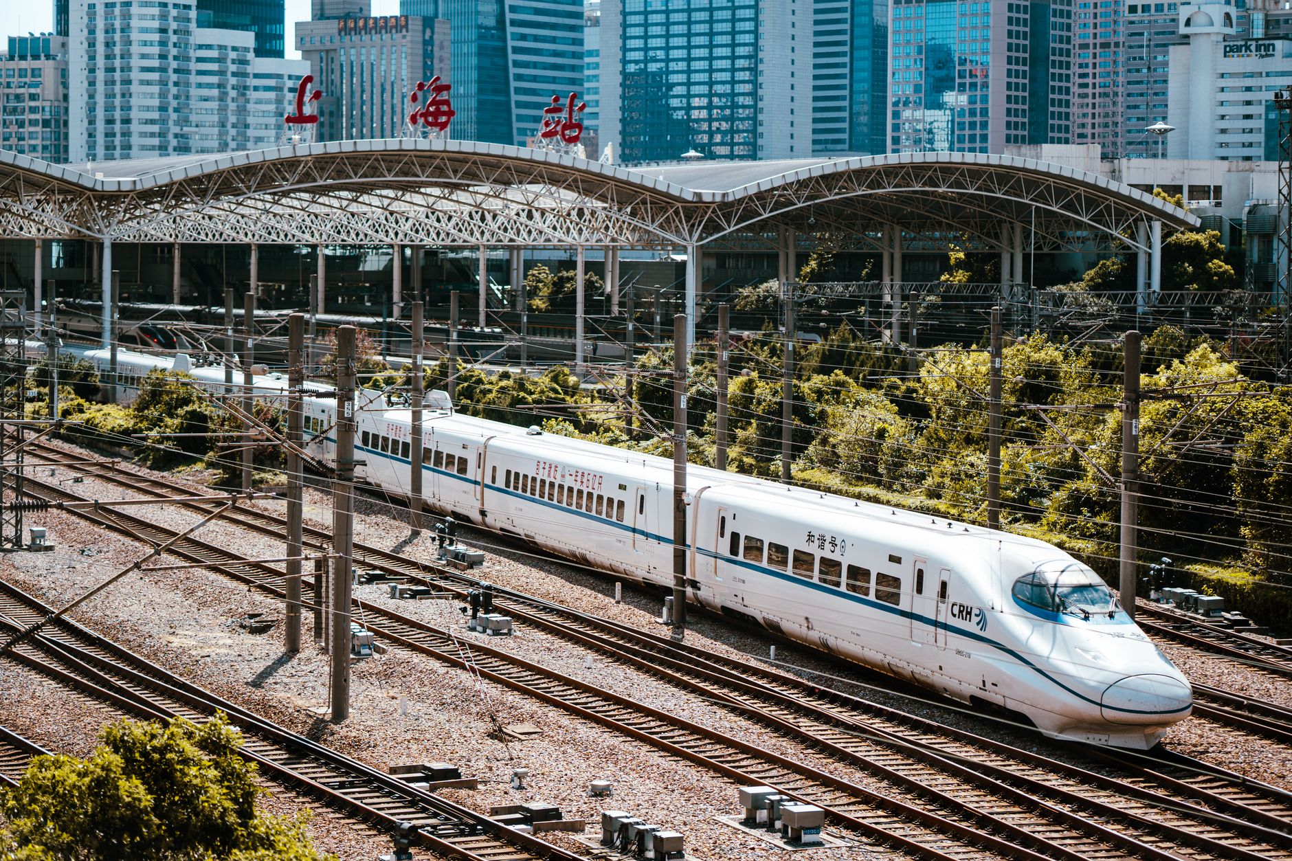 A high-speed train speeding through a dramatic, mountainous Chinese landscape shrouded in mist, with traditional architecture visible in the distance.