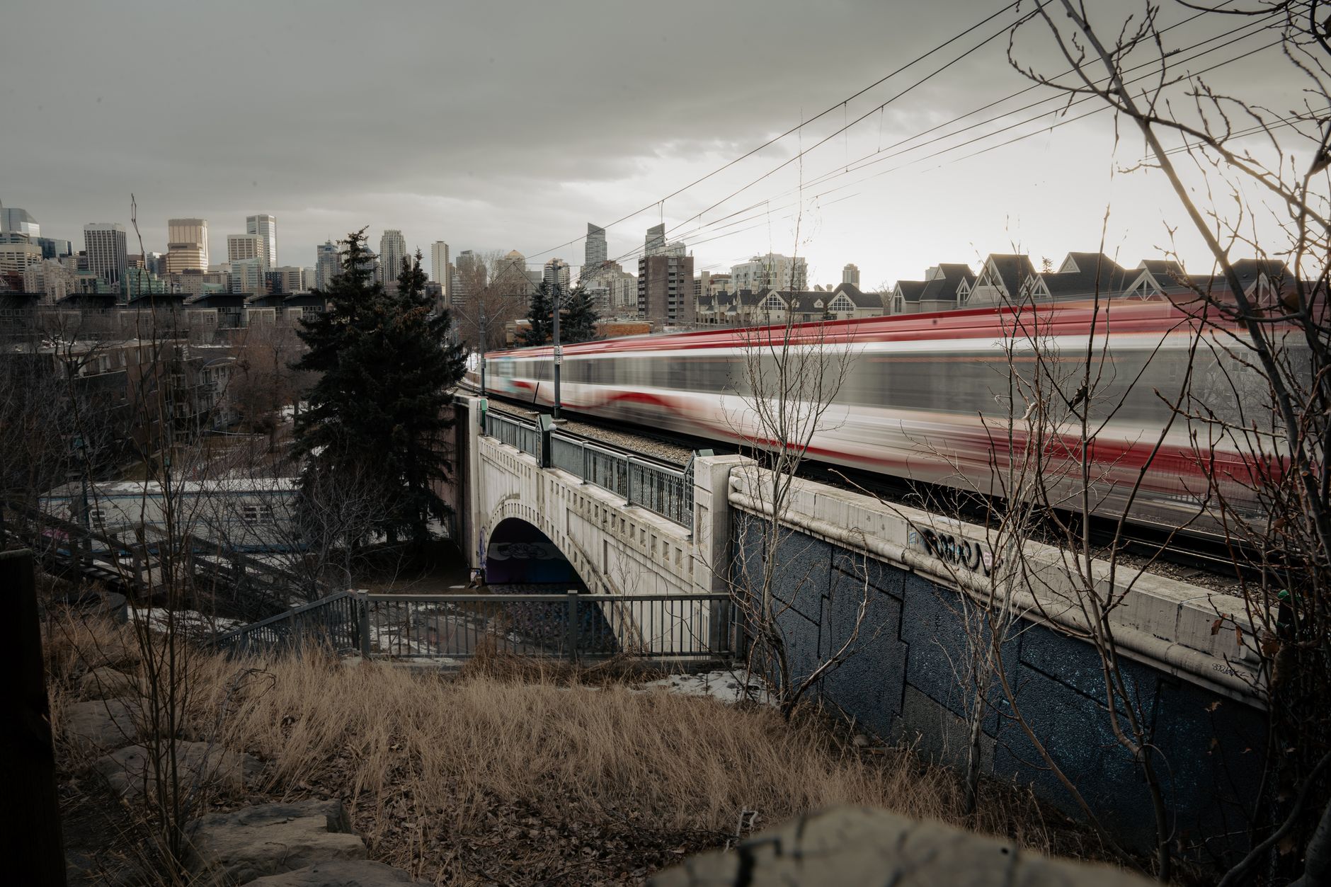 A modern high-speed train speeding through a picturesque Canadian rural landscape with autumn foliage, hinting at future connectivity between major cities and lesser-known regions.