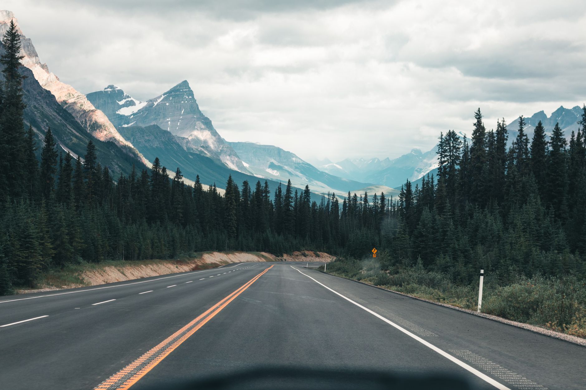 A long, straight stretch of the Trans-Canada Highway cuts through a vast, green forest under a wide, dramatic sky at sunrise.