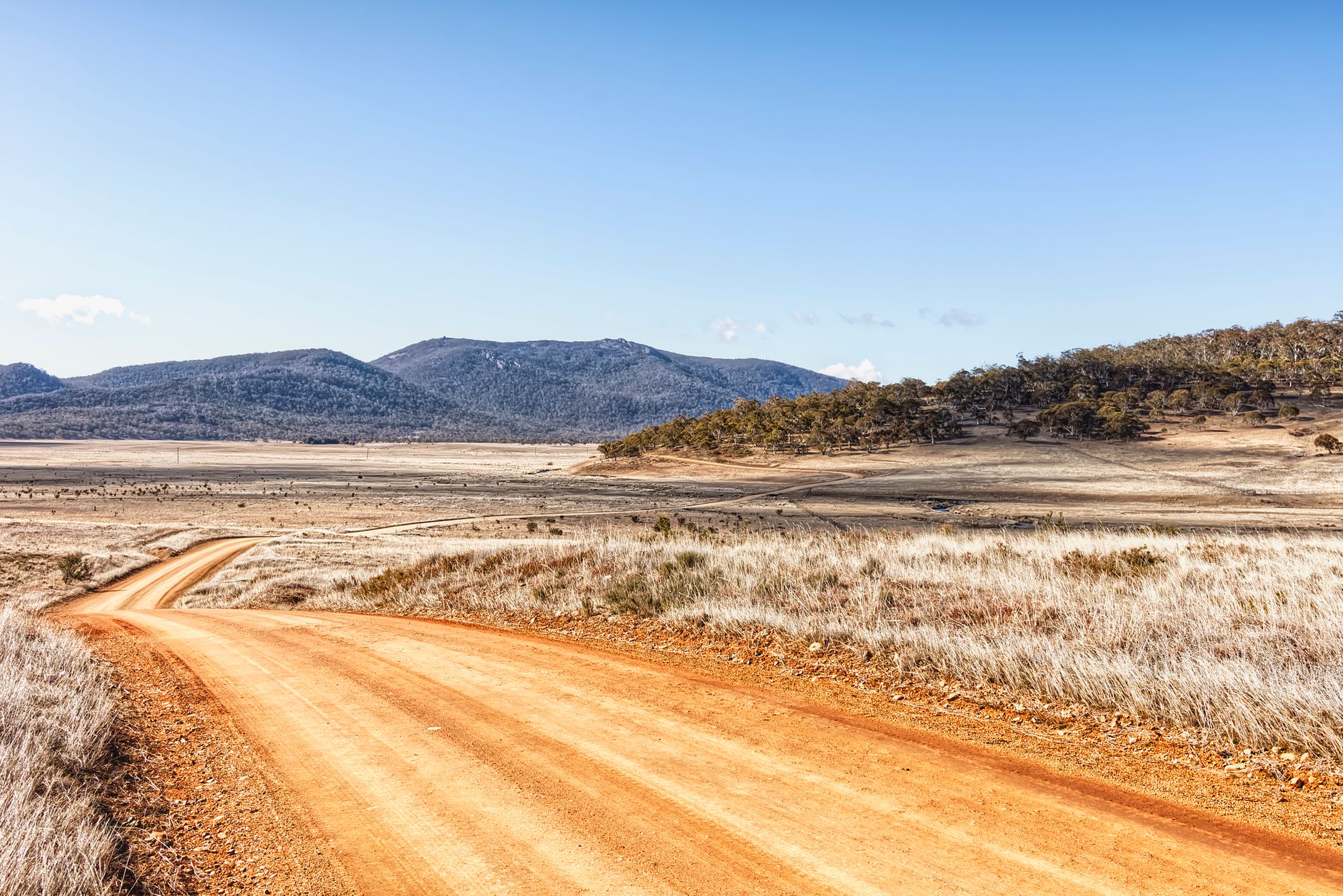 A lone car drives down a winding asphalt road through a vast, open landscape of rolling hills under a wide sky, symbolizing freedom and discovery.
