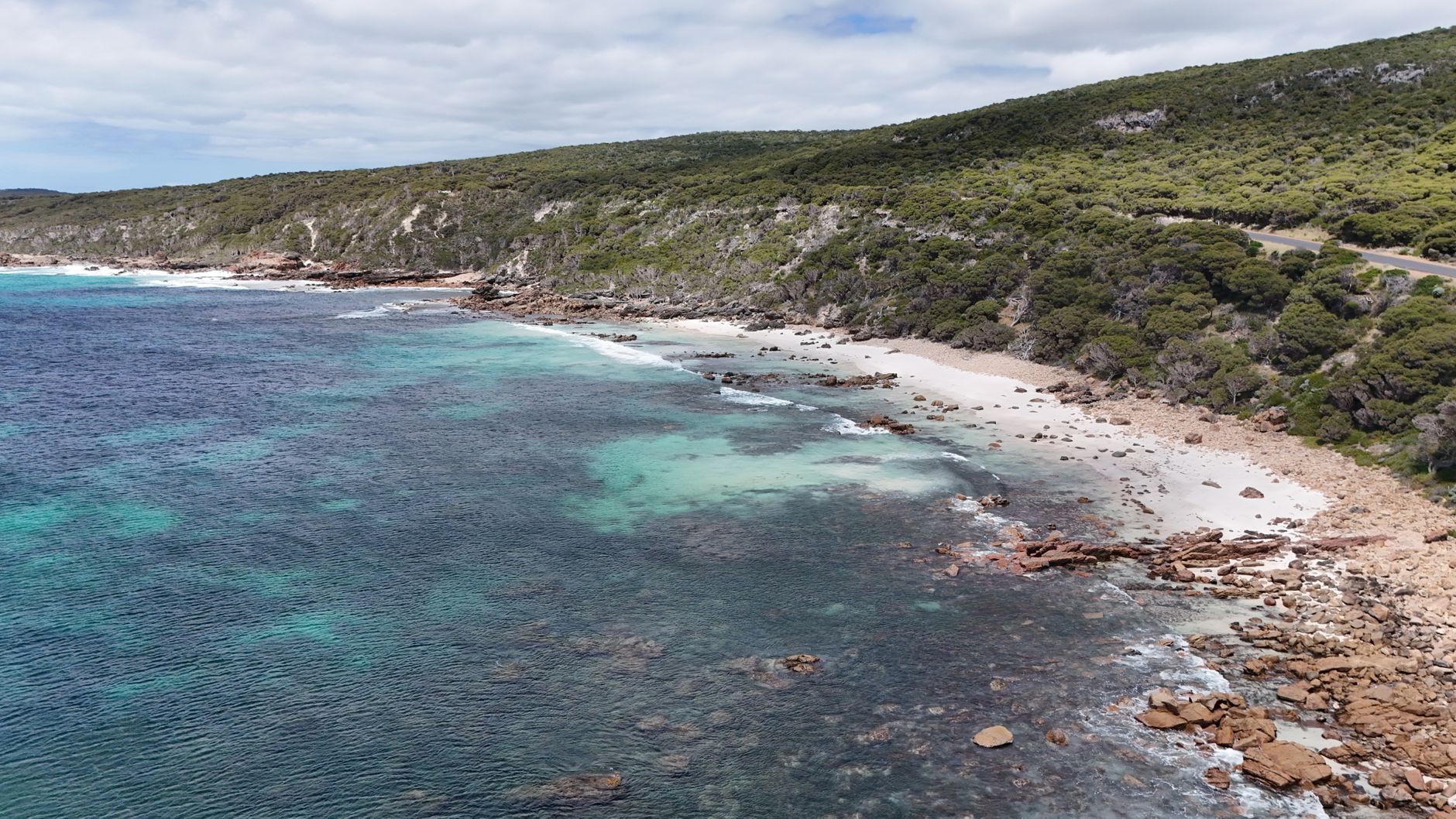 An aerial view of a pristine, untouched Australian beach with turquoise water, white sand, and dramatic cliffs under a clear blue sky.