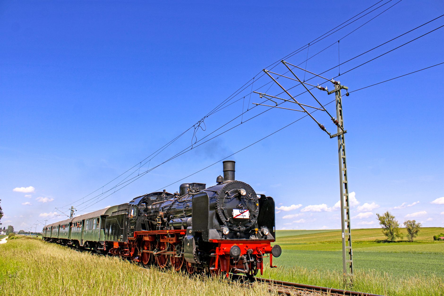 A sweeping view of a vintage steam train traveling through a vibrant autumn landscape in New Jersey, with historic tracks leading towards a distant old station.