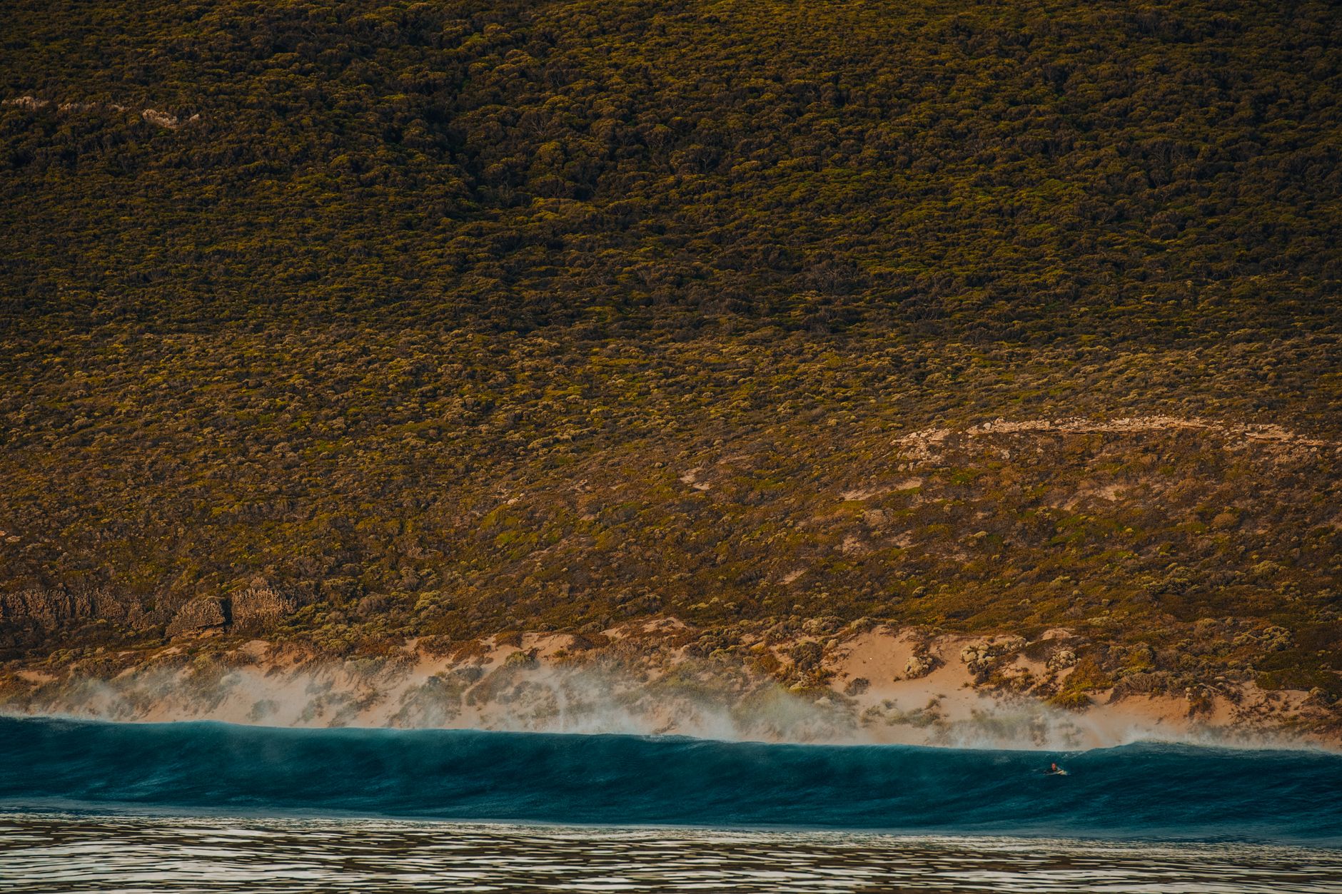 Sweeping aerial view of a dramatic, untouched coastline with waves breaking on a remote beach, hinting at undiscovered surf spots.