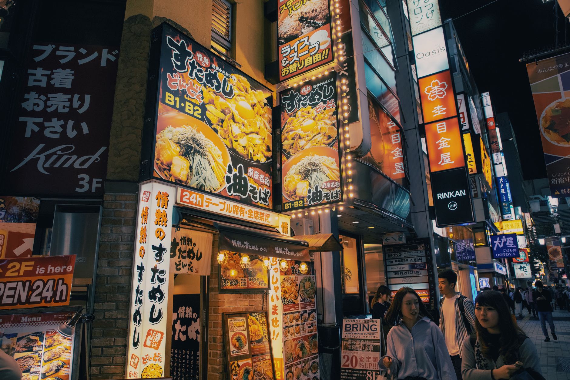 A vibrant, bustling night market scene in Tokyo, illuminated by lanterns and neon signs, with people enjoying street food.