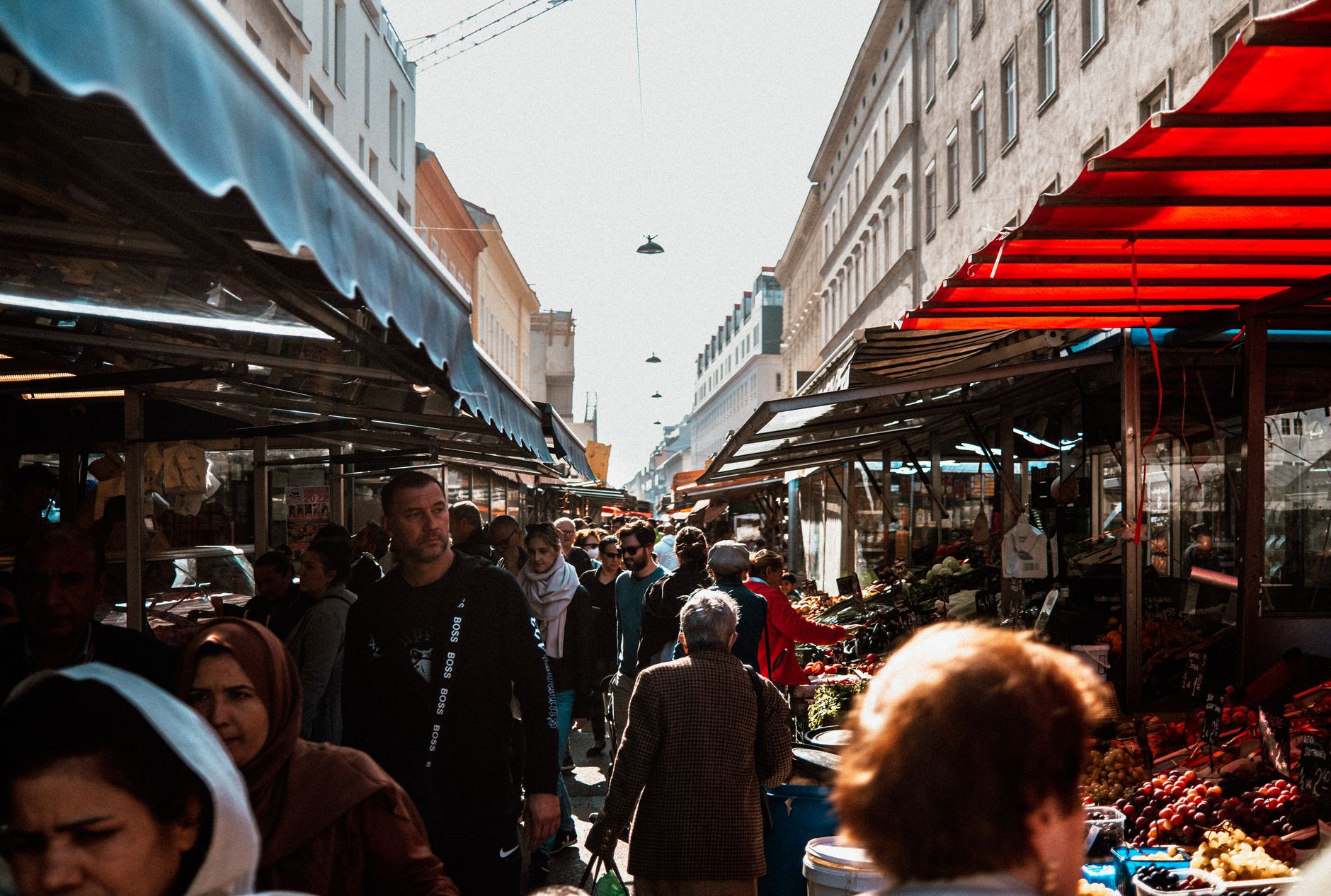 A vibrant overhead shot of an Austrian food market, showcasing fresh produce, cheeses, and charcuterie on wooden stalls, with a blurred background of people browsing.