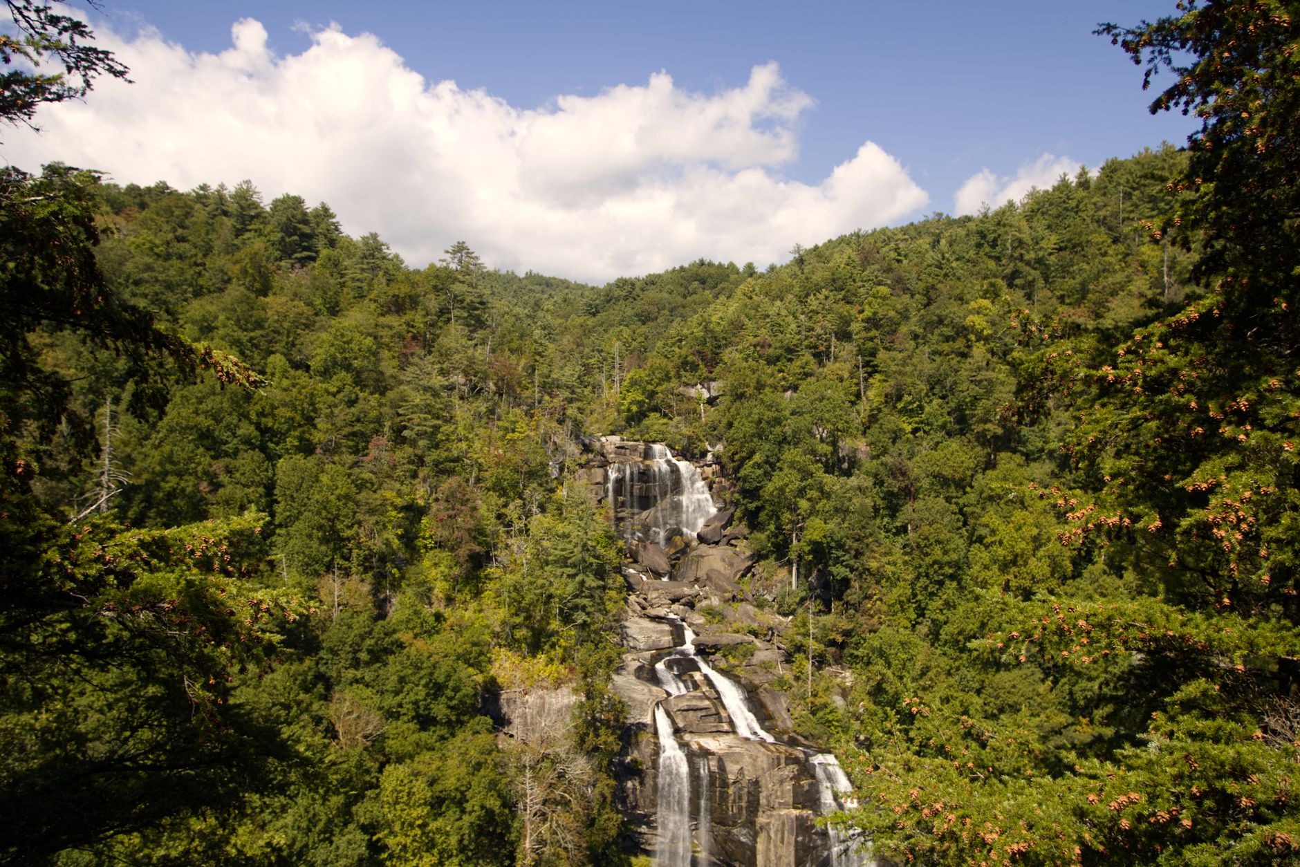 A sweeping panoramic view of misty, rolling blue ridges in the North Carolina mountains, with a tranquil river winding through a lush green valley in the foreground, evoking a sense of peaceful escape.