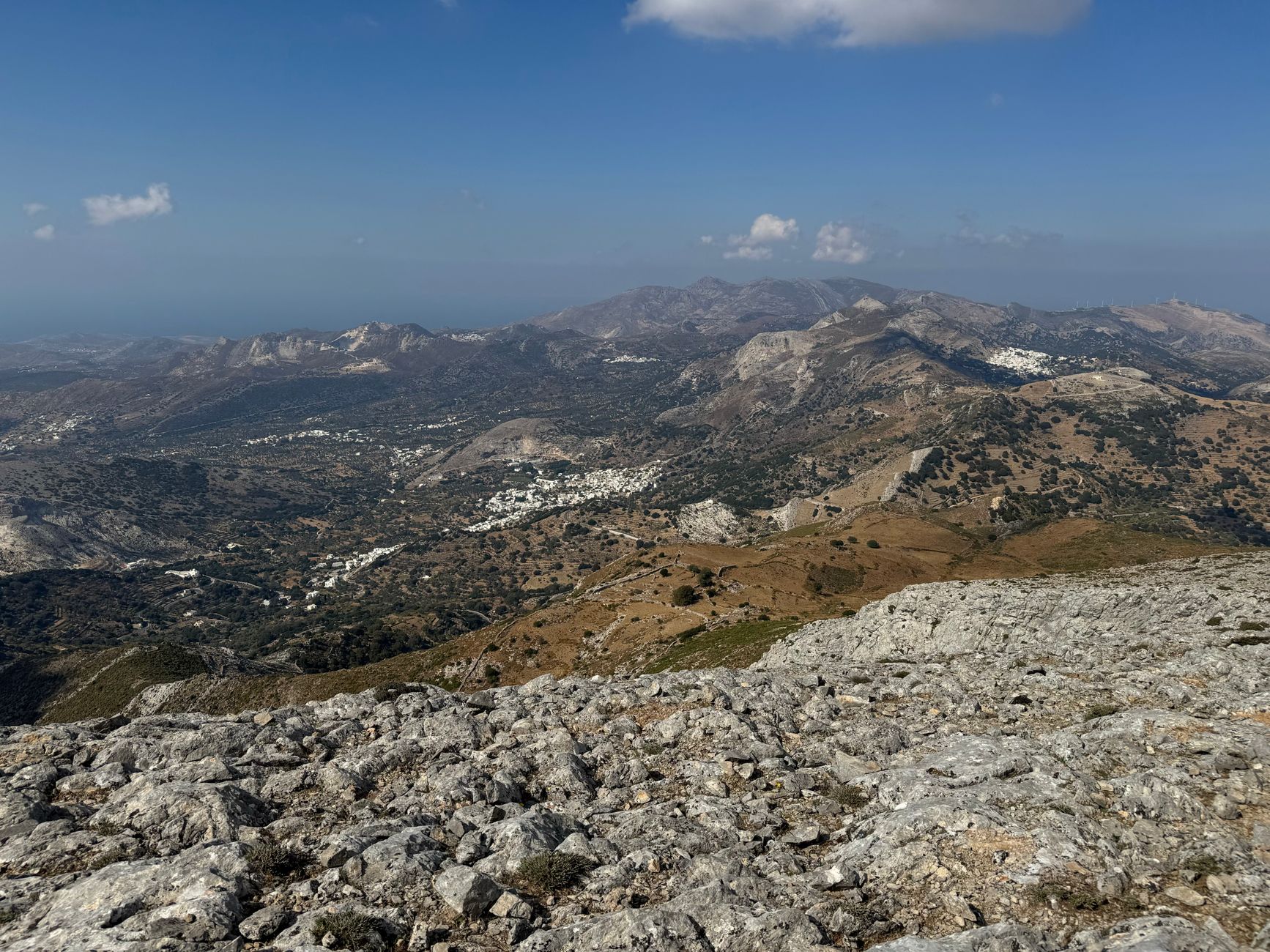 Sweeping panoramic view of a traditional Cretan village nestled in a rugged mountain landscape under a clear sky.
