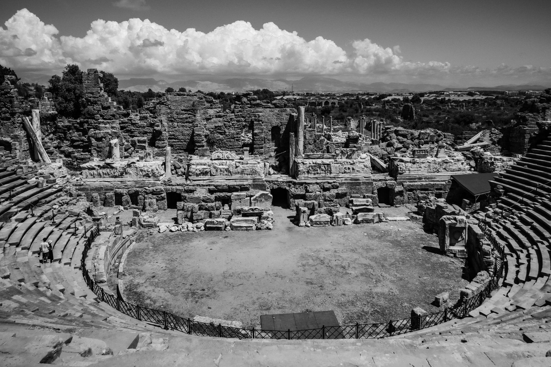 Panoramic view of ancient, weathered ruins nestled in a dramatic, sweeping landscape under a vast sky, evoking a sense of timeless mystery.