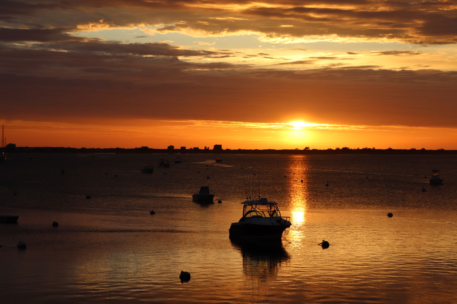 A wide-angle sunset view of Provincetown Harbor with fishing boats silhouetted against a colorful sky, hinting at the town's unique blend of natural beauty and maritime history.