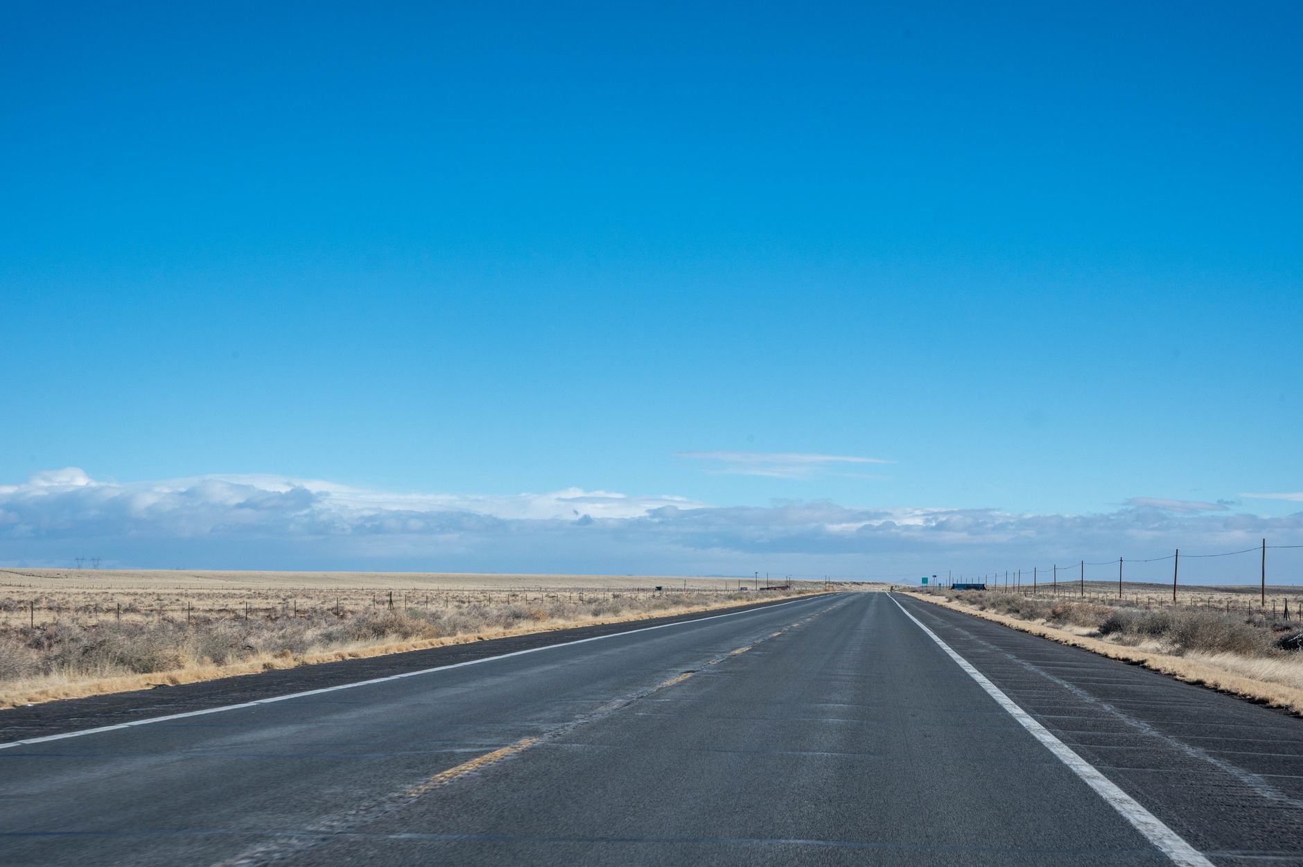A winding road cuts through a vast, diverse American landscape, transitioning from desert to mountains under a wide, dramatic sky, hinting at the expansive and varied terrain.