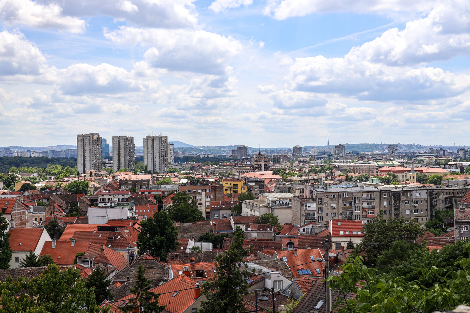 Sweeping panoramic view of Serbia's diverse landscape, featuring rolling green hills, a winding river, and distant ancient ruins under a clear sky.