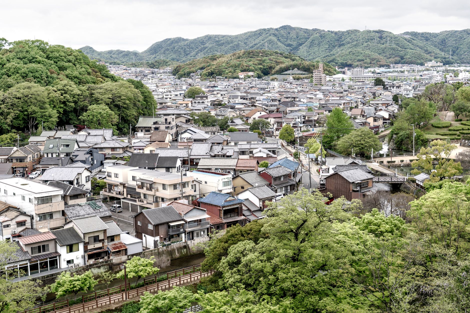 Sweeping aerial view of a verdant, mountainous Japanese countryside with a small, traditional village nestled in a valley, hinting at unseen stories.