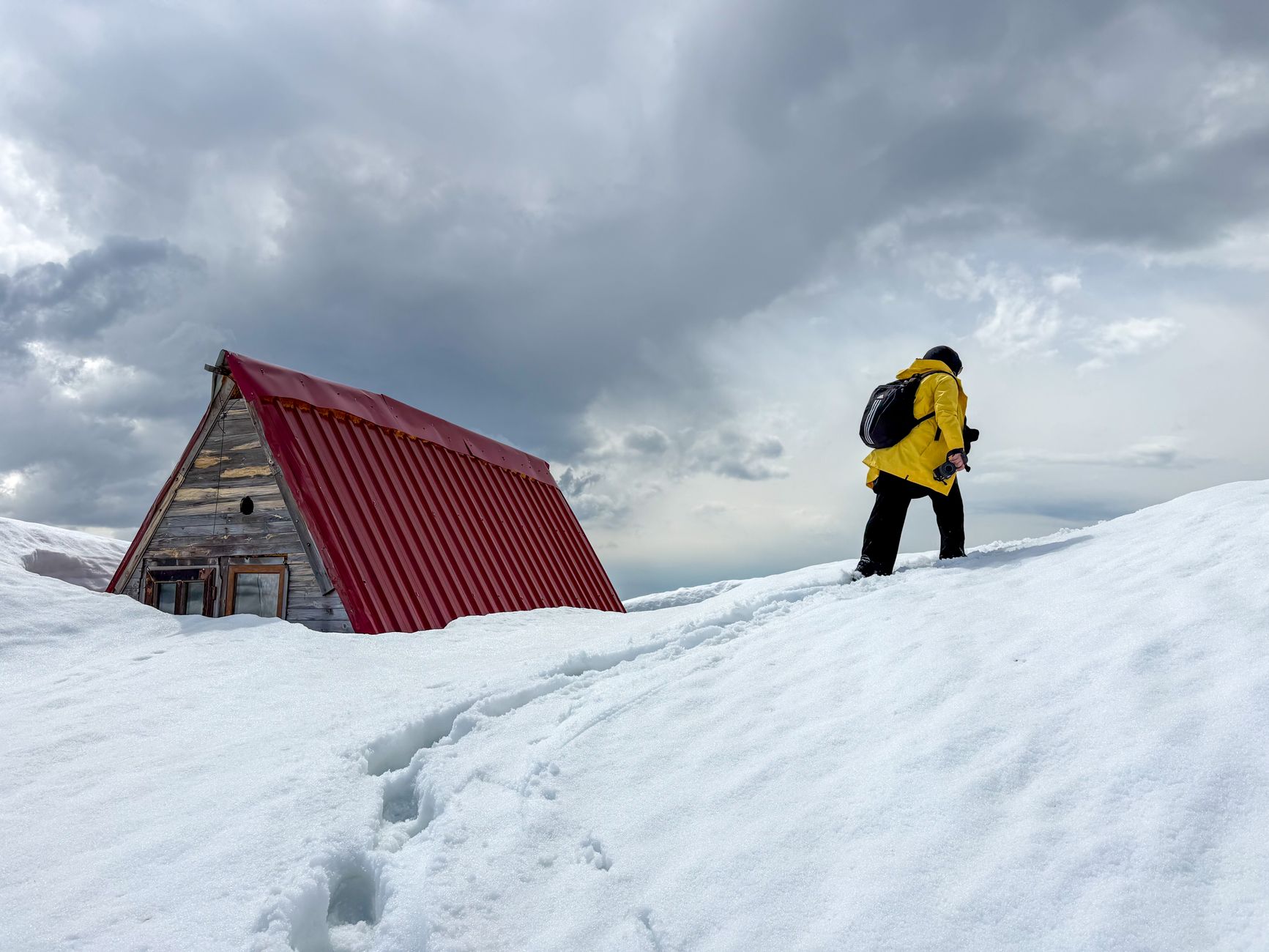 A minimalist tarp shelter pitched on a remote, rugged mountain ridge at sunrise, with a backpack leaning nearby.