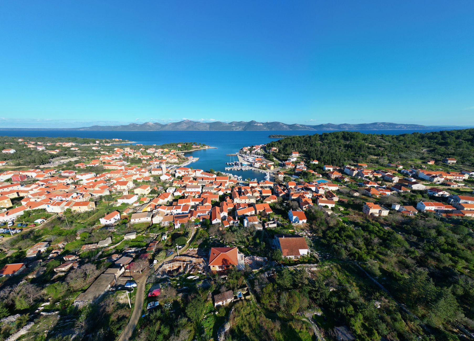 Sweeping drone shot of the dramatic Croatian Adriatic coastline at sunset, with islands, turquoise waters, and ancient stone structures visible.