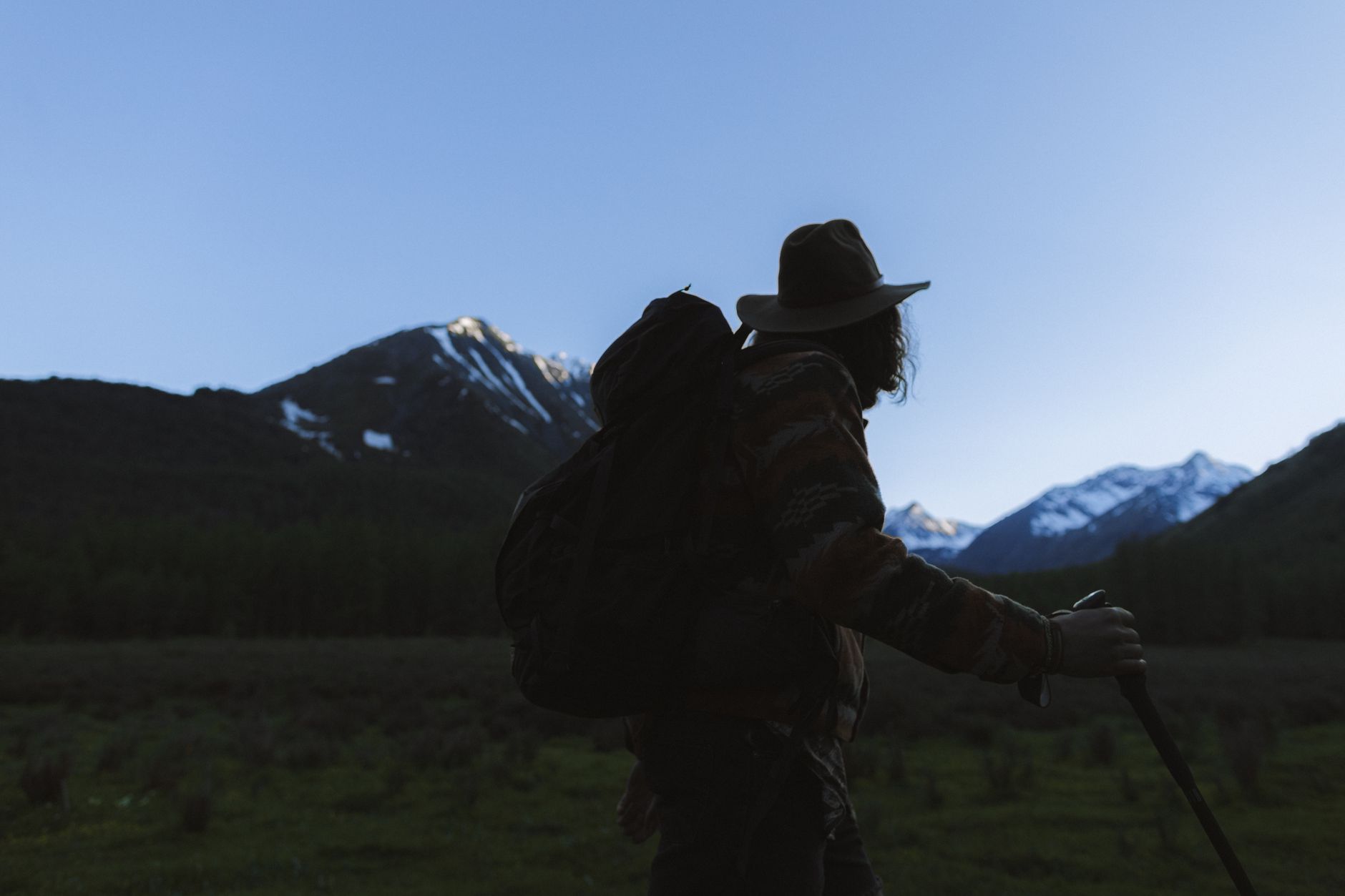 A solitary backpacker with a small pack watching the sunrise over a vast, dramatic mountain range, symbolizing remote adventure and alternative shelter.