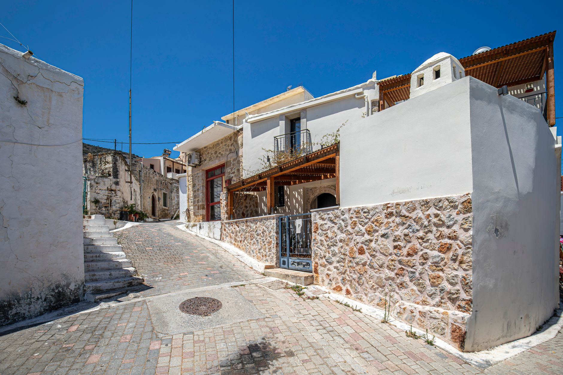 A panoramic view of a traditional Cretan village nestled in a valley, surrounded by olive groves and distant mountains under a clear blue sky, evoking a sense of timelessness.