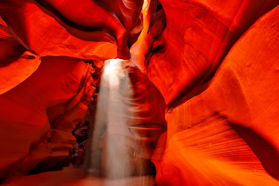 Dramatic light beams piercing through the narrow, sculpted sandstone walls of Antelope Canyon, illuminating the reddish-orange rock formations.