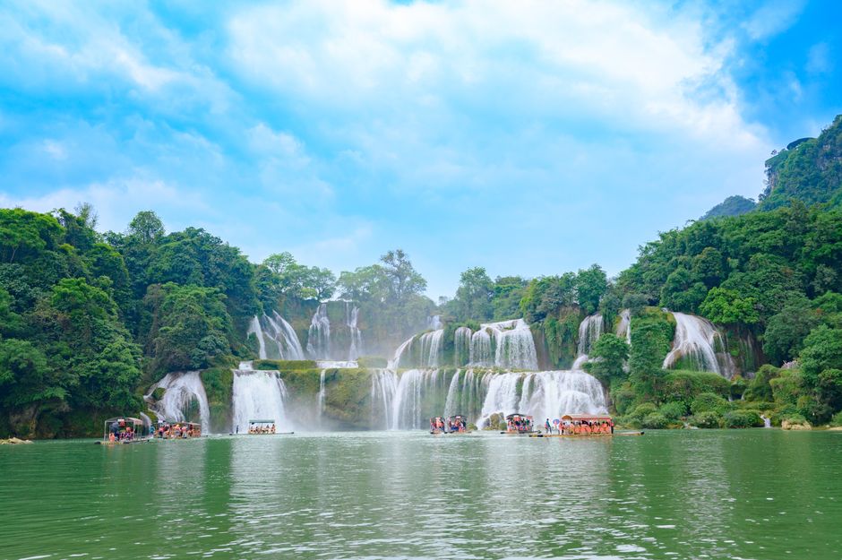 Panoramic view of Ban Gioc Waterfall, a majestic multi-tiered cascade forming the border between Vietnam and China, surrounded by lush green karst mountains.