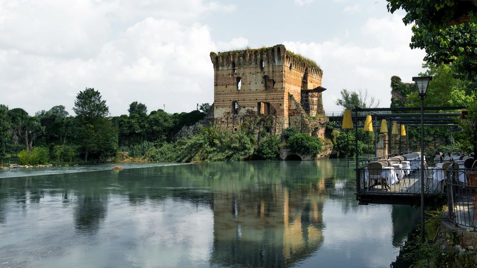 Panoramic view of Borghetto sul Mincio, a medieval Italian village with historic watermills along the Mincio River, under a clear sky.