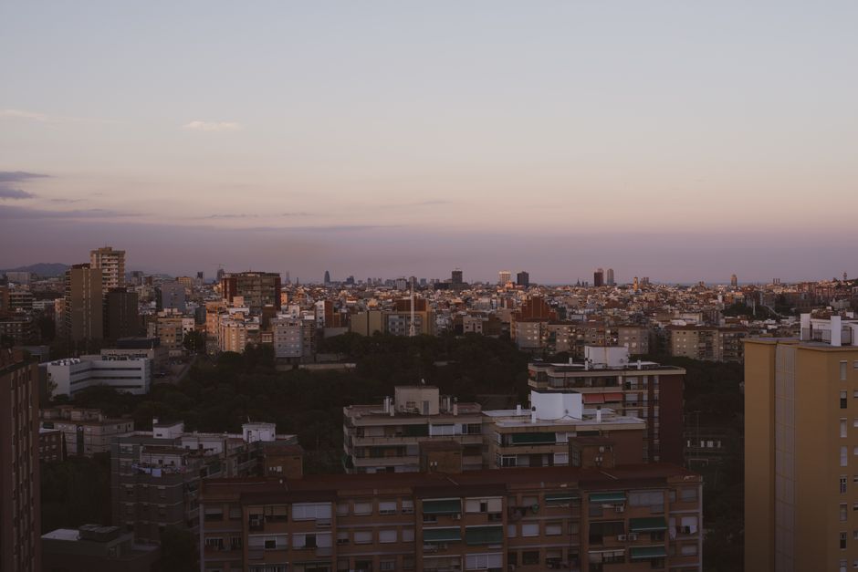 Panoramic view of Barcelona from Bunkers del Carmel at sunset, showing the sprawling city, Sagrada Familia, and the Mediterranean Sea under a colorful sky.