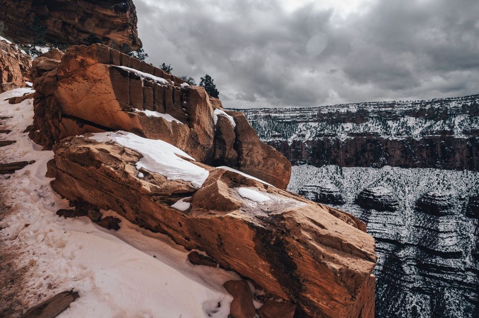 A wide, panoramic view of the Grand Canyon at sunset, showing vast red and orange rock formations under a dramatic sky with deep shadows.