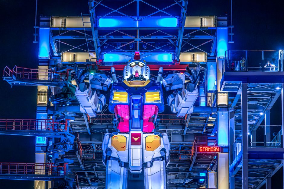Giant white and red RX-0 Unicorn Gundam statue standing tall outside DiverCity Tokyo Plaza in Odaiba, Japan, against a modern building backdrop at dusk.