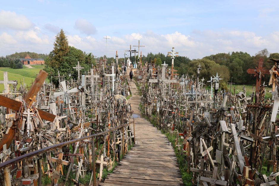 Panoramic view of the Hill of Crosses in Lithuania, showing hundreds of thousands of wooden and metal crosses densely packed on a low mound under a dramatic sky.