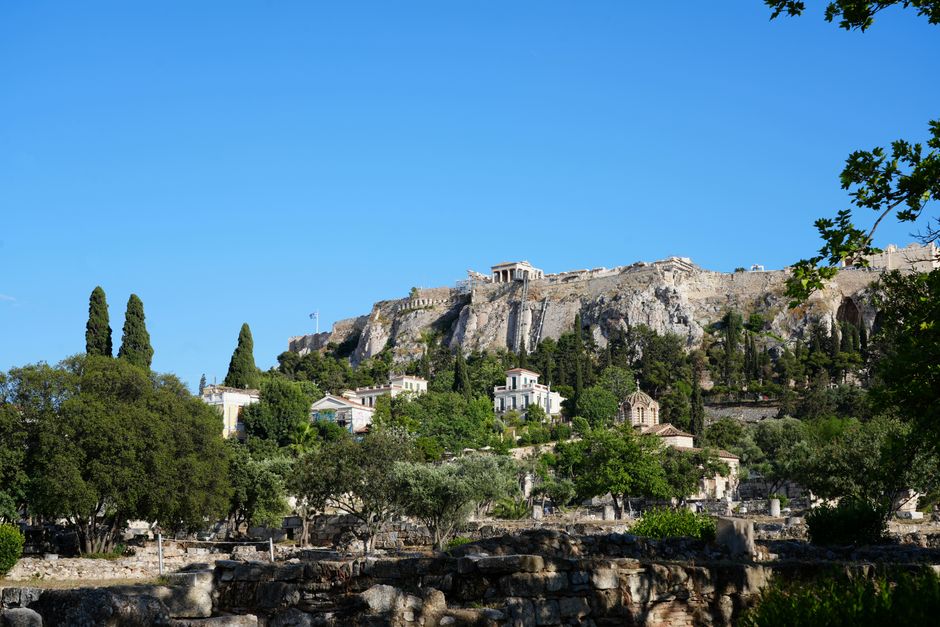 Panoramic view of the ancient Kerameikos Cemetery in Athens, Greece, with scattered ruins, funerary stelae, and the Eridanos River, under a clear sky.
