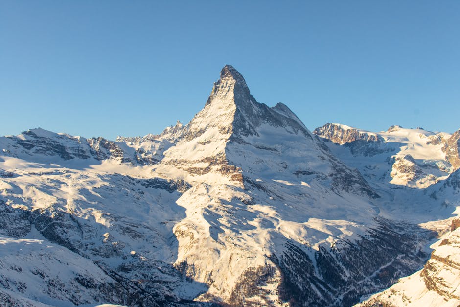 Panoramic view of the iconic Matterhorn peak towering over the Swiss Alps, with lush green valleys and Zermatt in the distance.
