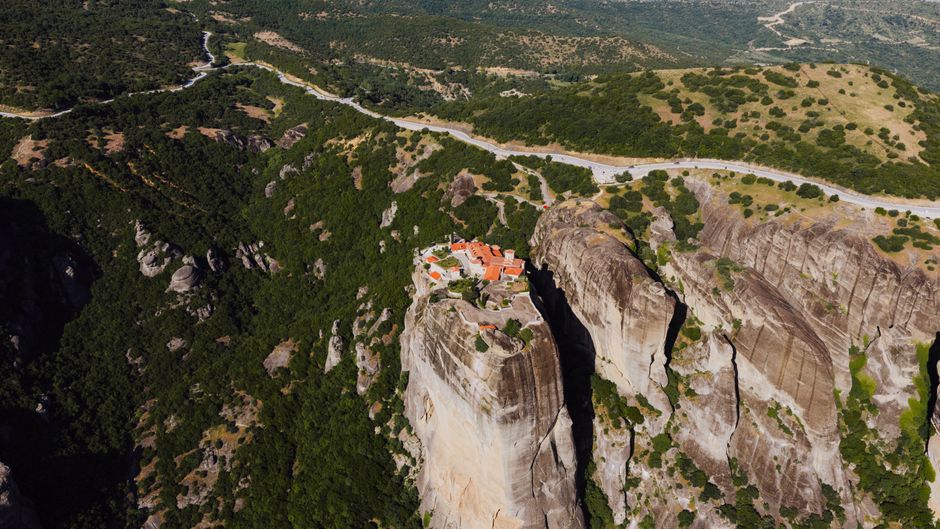 Panoramic view of the Meteora Monasteries in Greece, showing ancient buildings perched atop towering, dramatic sandstone rock formations under a clear sky.