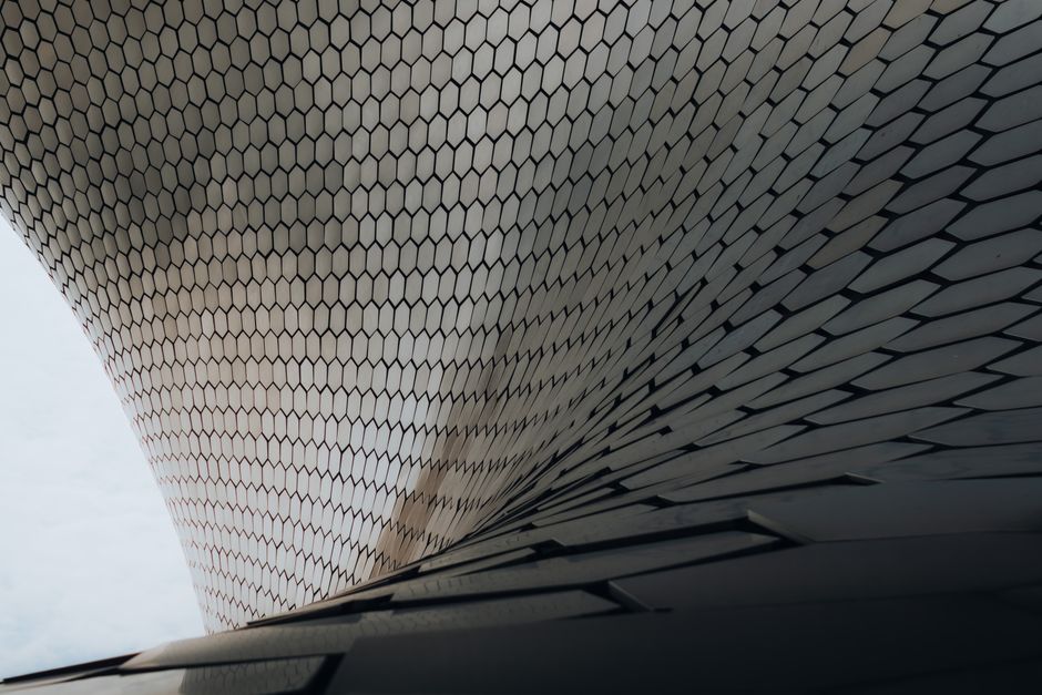 Striking exterior of Museo Soumaya in Mexico City, featuring its distinctive curved, shimmering facade covered in thousands of hexagonal aluminum tiles, reflecting the sky.
