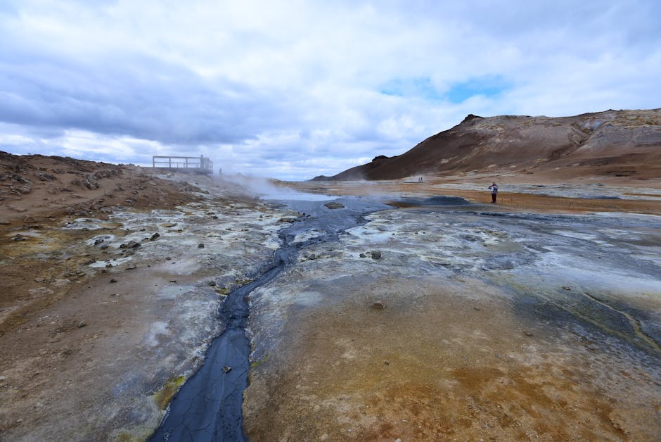 Aerial view of Lake Mývatn, Iceland, showing vibrant blue water, green pseudo-craters, and steam rising from geothermal areas under a dramatic sky.