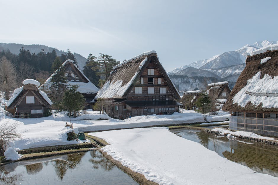 Snow-covered traditional gassho-zukuri houses in Shirakawa-go, Japan, with smoke rising from chimneys and a serene winter landscape.