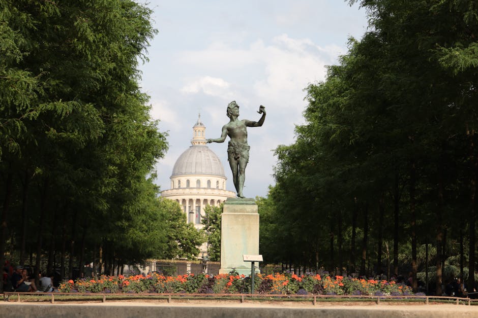 View of the Square du Vert-Galant in Paris, showing the equestrian statue of Henri IV surrounded by trees, with the Seine River and bridges in the background under a soft sky.