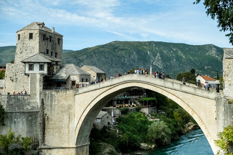 The iconic Stari Most bridge in Mostar, Bosnia and Herzegovina, illuminated at sunset with its elegant stone arch reflecting in the calm, green Neretva River, surrounded by historic buildings.