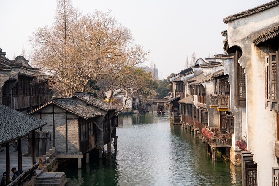 Traditional wooden buildings and stone bridges lining the tranquil canals of Wuzhen Water Town at dusk, with reflections on the water.